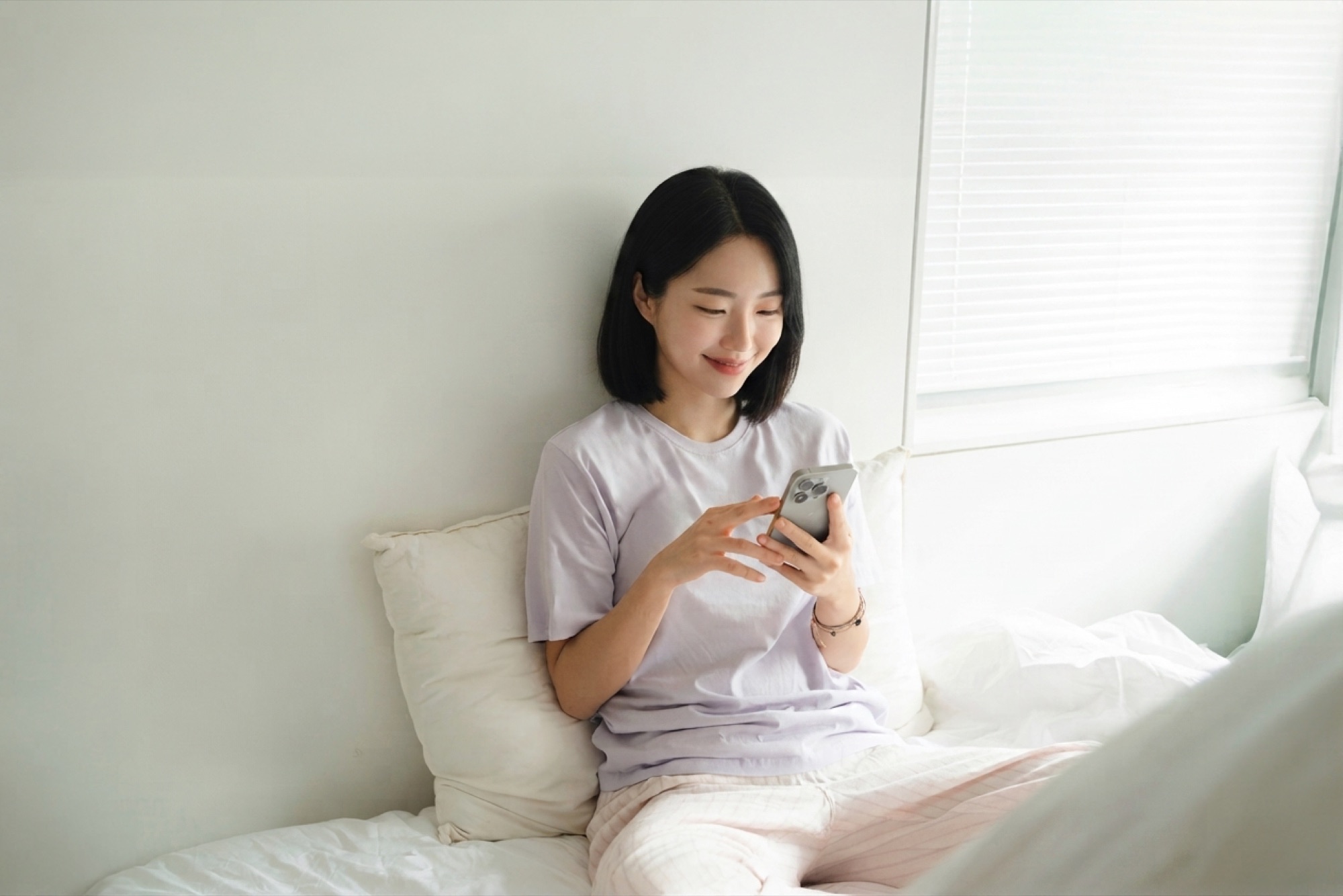 침대에서 스마트폰으로 빈방 알림을 확인하는 모습